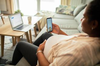 Pregnant woman using a nutrition app on her phone while sitting on a couch in the livingroom.