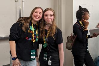 Two female youth standing next to each other, smiling. 