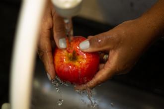 A red apple being washed with water under a faucet.