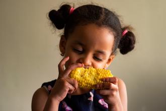 Young girl eating corn on the cob.