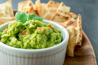Homemade guacamole in a ramekin with pita chips in the background.