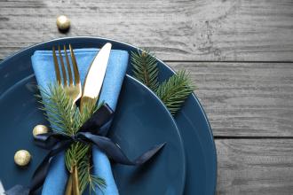 Winter table setting with blue plates, blue napkin, silverware, and pine tree sprigs